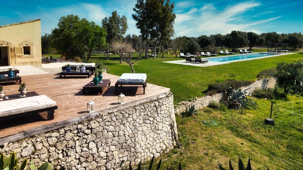Un espace aménagé au bord de la piscine, avec des chaises longues, un mur en pierre et une vue sur la piscine.