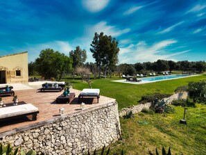 Un espace aménagé au bord de la piscine, avec des chaises longues, un mur en pierre et une vue sur la piscine.