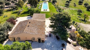 Une villa avec un toit en tuiles, une piscine et un jardin planté d’oliviers.