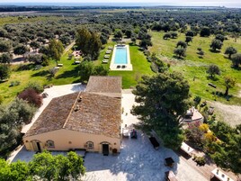 Una villa con techo de tejas, piscina y jardín con olivos.