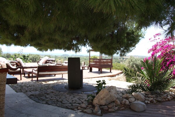 An outdoor seating area with stone flooring, wooden furniture, and a view of the landscape. - Terre di Vendicari (Noto)