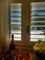 Una habitación con una mesa dispuesta para dos personas, que incluye una botella de champán, dos copas de vino, un cuenco de fresas y un jarrón con flores.