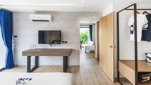Une chambre moderne avec un mur en briques, un téléviseur à écran plat, une table en bois et une armoire où sont suspendus des vêtements.