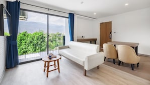 Un salon moderne comprenant un canapé, deux fauteuils, une petite table et un balcon offrant une vue sur la verdure et les montagnes.