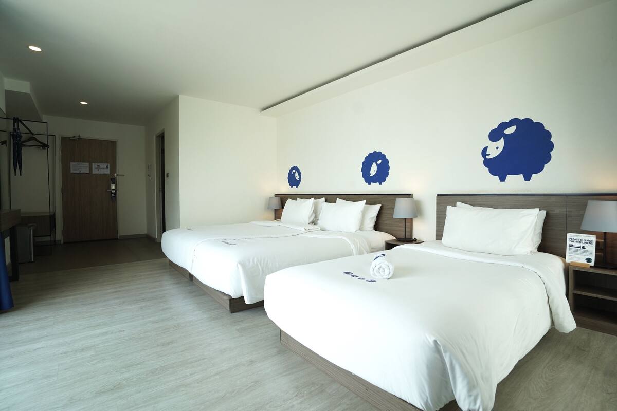 Ein Hotelzimmer mit zwei Betten, Holzboden und einer Wand mit Schafstickern.