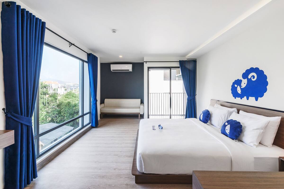 Ein Hotelzimmer mit einem großen Bett, einer Sitzecke und Blick auf die Stadt.