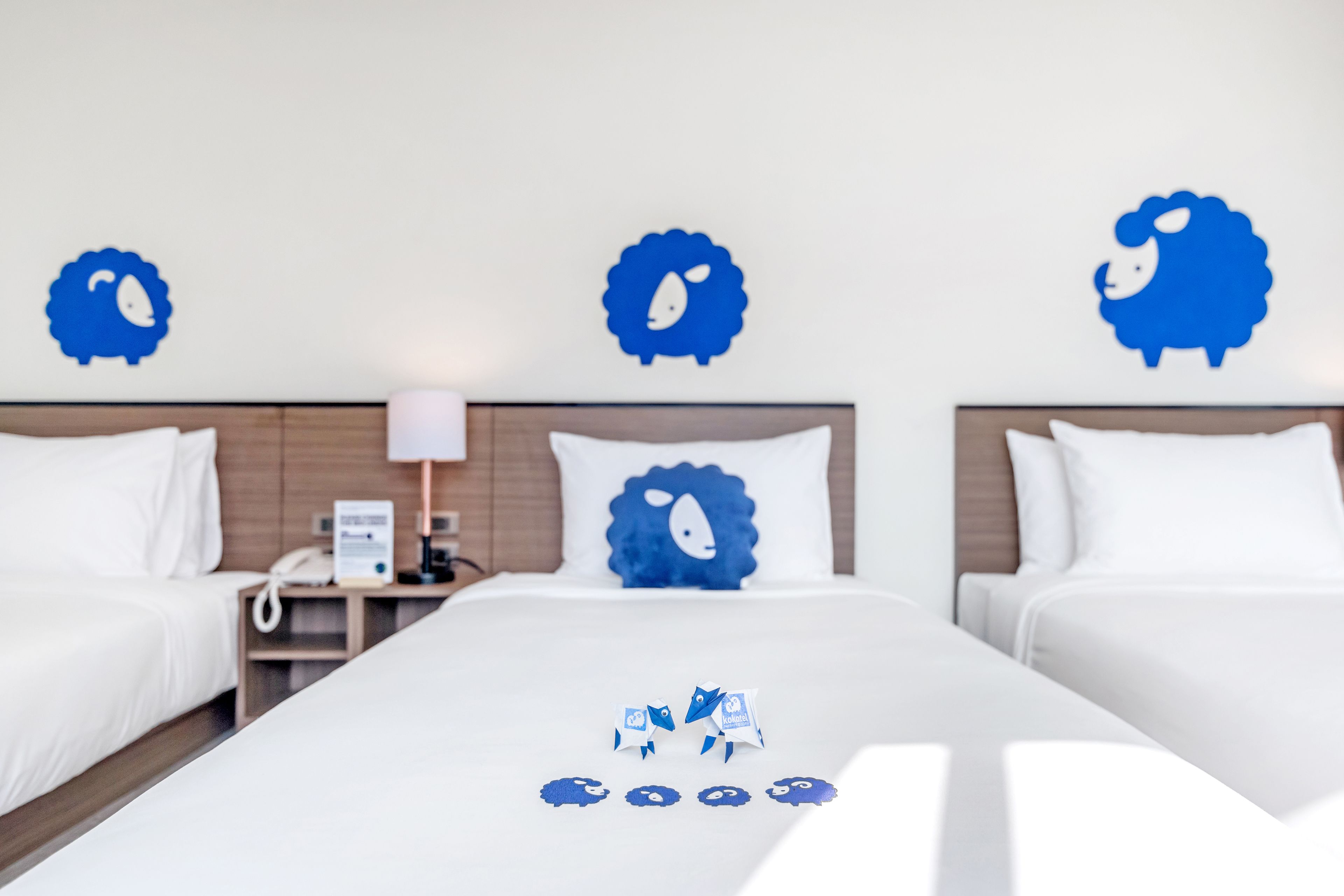 Habitación de hotel con dos camas, ropa de cama blanca y decoración azul en las paredes.