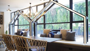 Un coin salon confortable avec une table et des chaises, de grandes fenêtres donnant sur un paysage verdoyant et un lustre moderne.