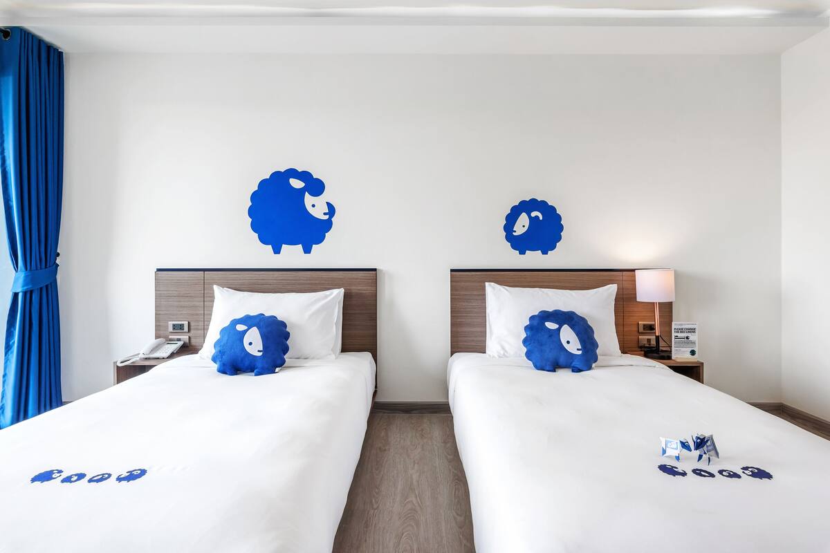 Ein Hotelzimmer mit zwei Betten, jedes mit einem blauen Kopfkissen und einer Wanddekoration.