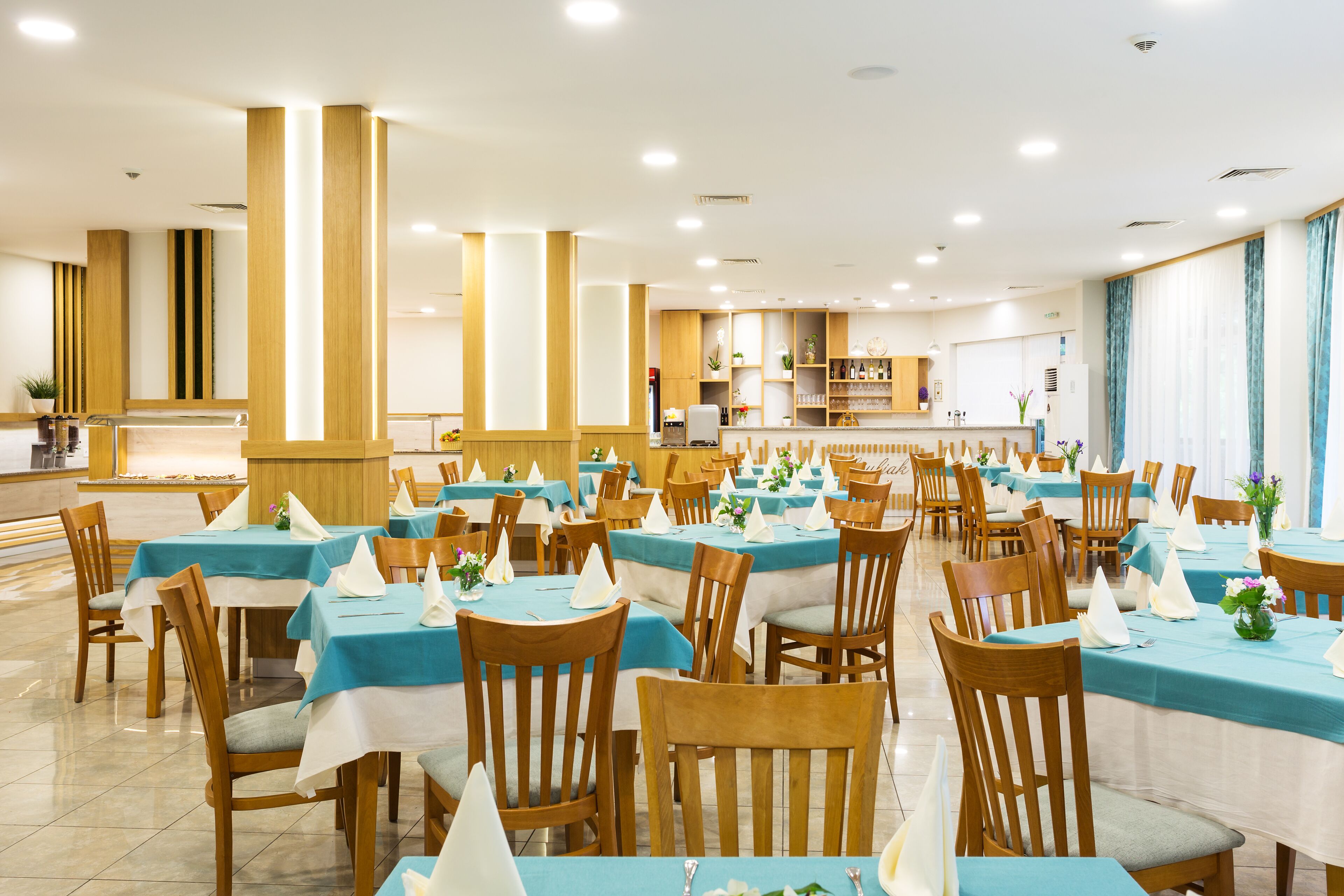 A spacious dining area with multiple tables and chairs, a counter, and a kitchen in the background.