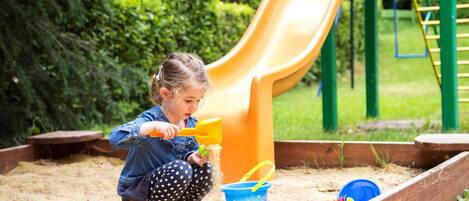A child playing with sand near a playground slide.