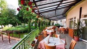An outdoor patio with tables and chairs, surrounded by potted plants and a green railing. - Ljuljak (Golden Sands)