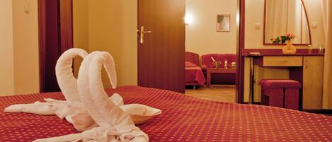 Ein Hotelzimmer mit rotem, gemustertem Bettbezug, einer Holztür, einem roten Sessel, einem kleinen Tisch mit einer Vase und einem Spiegel an der Wand.