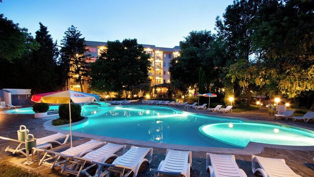 A swimming pool with lounge chairs and umbrellas, surrounded by trees and a building in the background. - Ljuljak (Golden Sands)