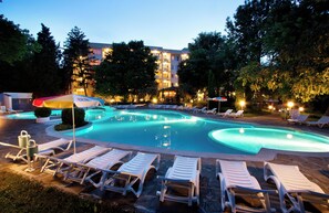 A swimming pool with lounge chairs and umbrellas, surrounded by trees and a building in the background. - Ljuljak (Golden Sands)