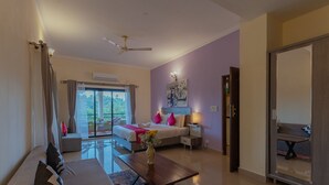 A hotel room with a bed, a sofa, a dining table, and a balcony with a view of greenery. - TreeHouse Blue Hotel & Villas (Colva)