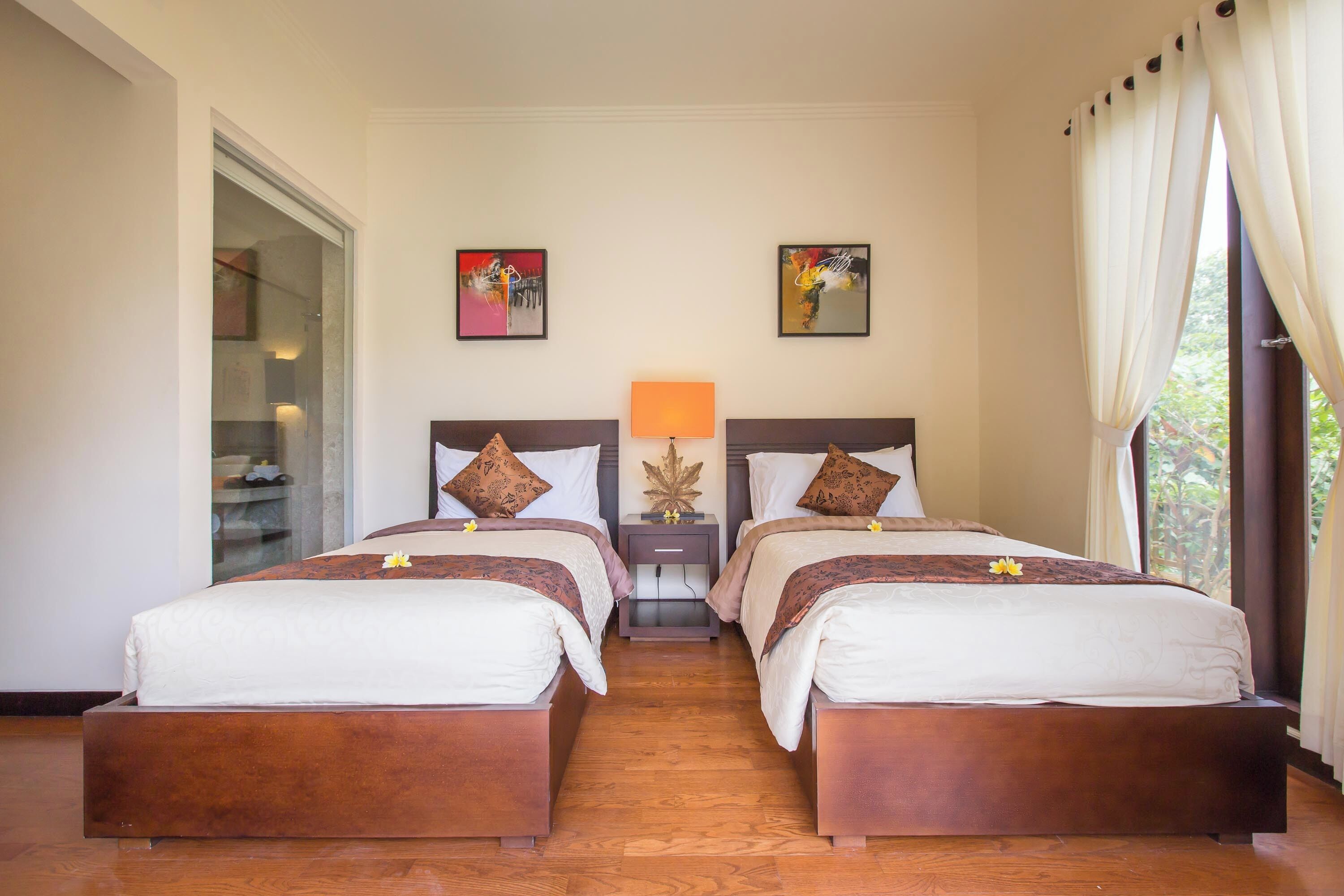 A hotel room with two beds, a nightstand with a lamp, and artwork on the walls.
