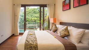 Habitación de hotel con una cama grande, una mesita de noche, una lámpara y vistas a una piscina y vegetación.