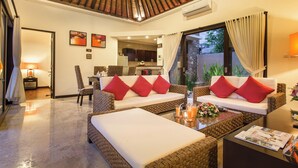Amplia sala de estar con techo alto, dos sofás con cojines rojos, una mesa de centro y vistas a la cocina y al área exterior.