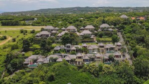 Zona residencial con varias casas, algunas con piscinas, rodeada de vegetación y colinas al fondo.