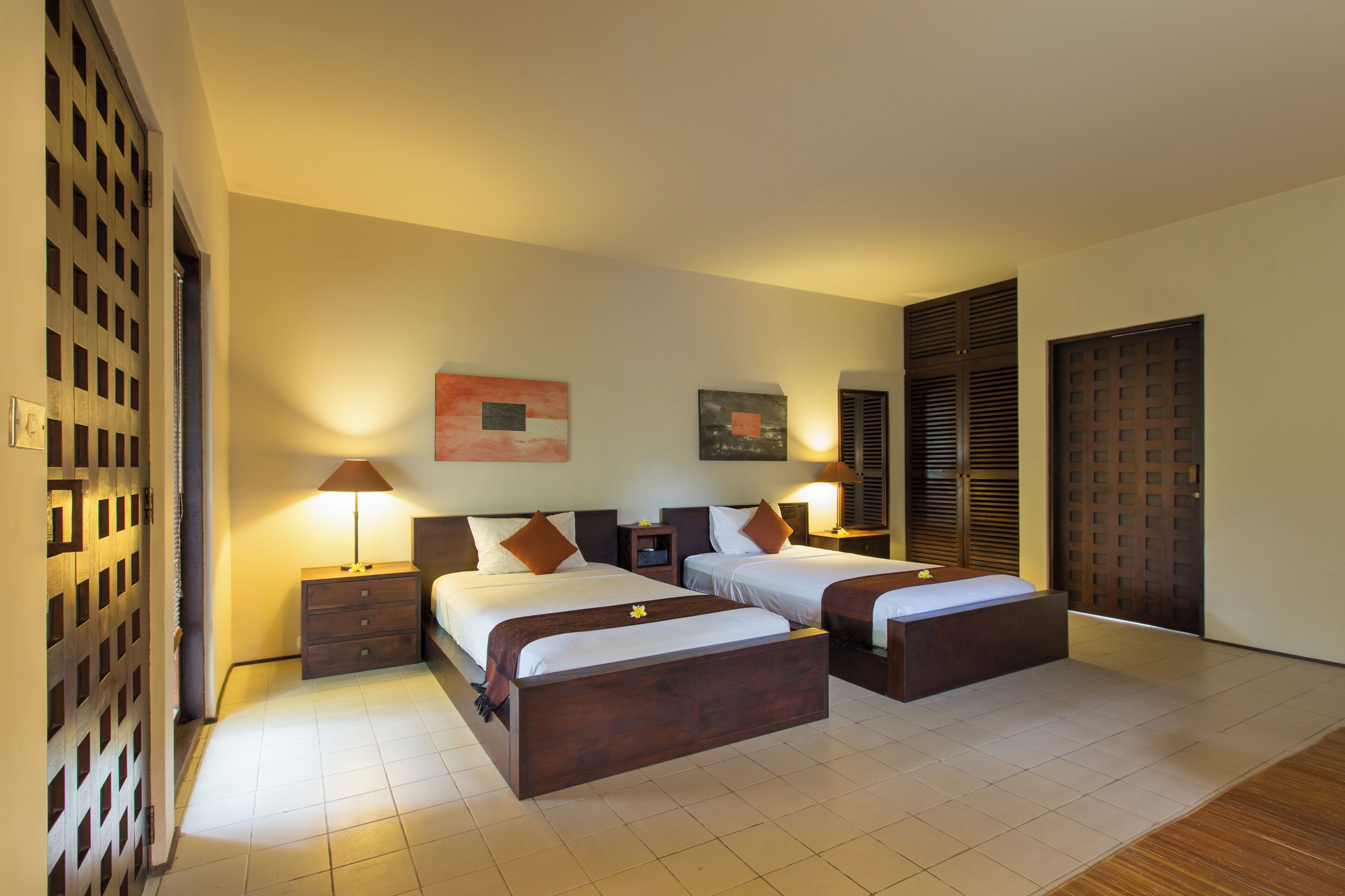 A hotel room with two beds, a wooden floor, and a large window.