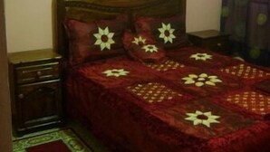 A bedroom with a wooden bed, a nightstand, a bedside table, a window with curtains, and a patterned rug. - Appartement 2 Chambre Ville Nouvelle Fes (Fes)