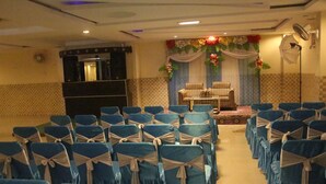 Un salón de conferencias con filas de sillas, un escenario con decoración floral y un sistema de sonido.