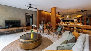 A modern living room with a television, round coffee table, sofas, and a dining area with a bar. - Jadine Bali Villa by Nagisa Bali (Canggu)