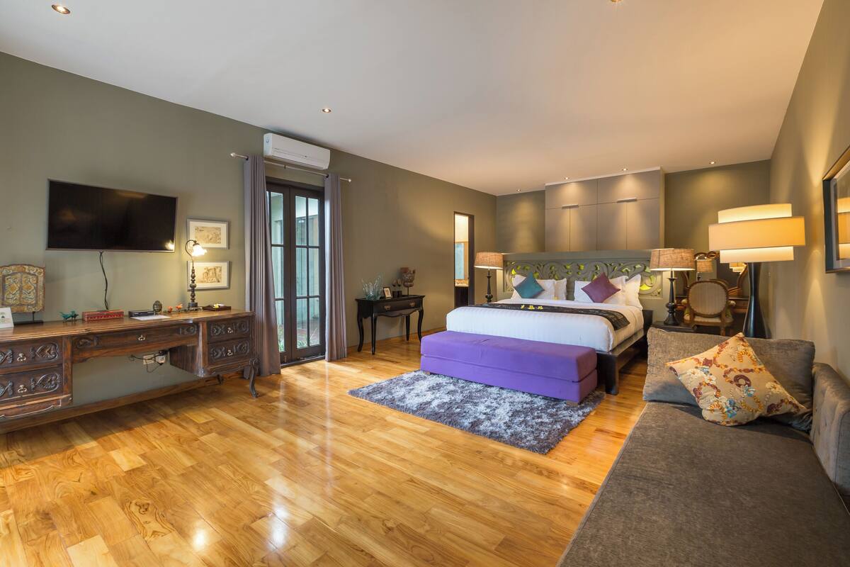 A bedroom with a bed, a desk, a TV, and a sofa.