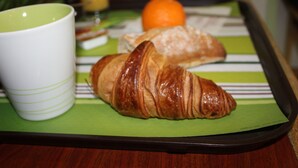 Uma bandeja com um croissant e uma laranja sobre uma toalha xadrez.