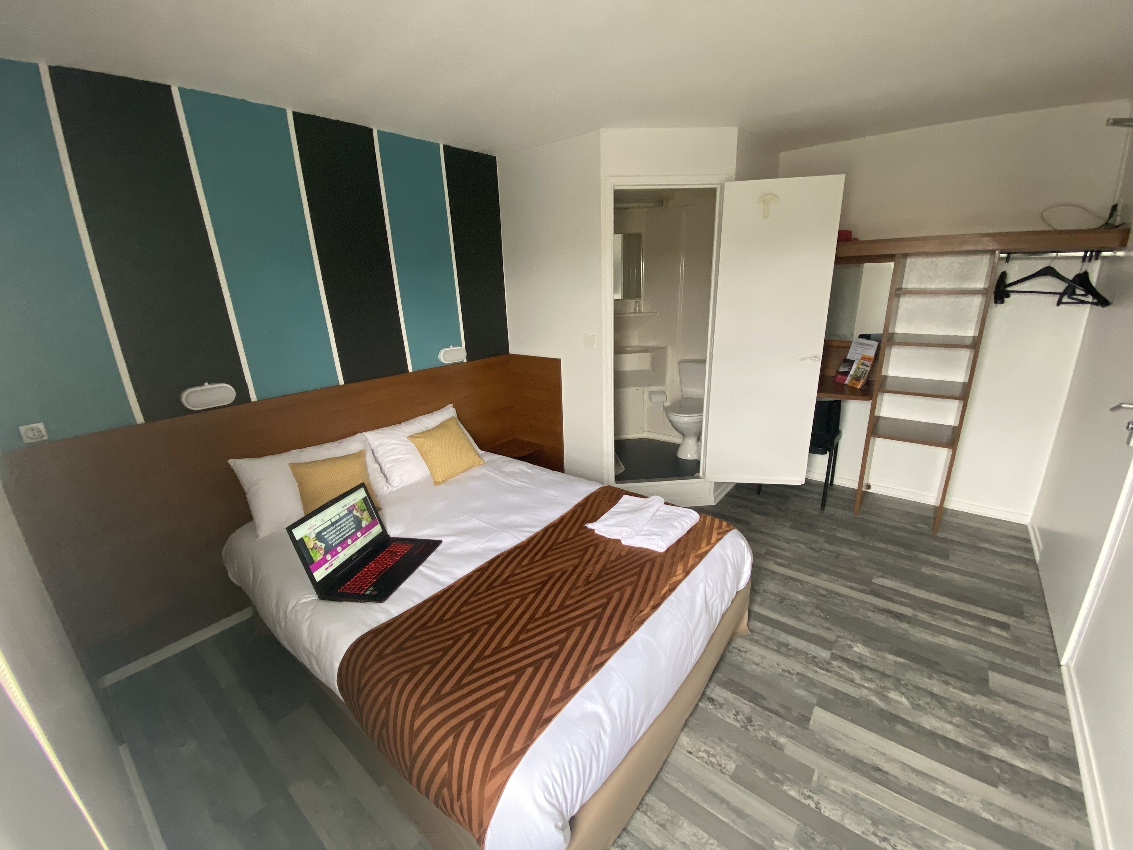 Habitación de hotel con cama, un ordenador portátil sobre la cama, armario y baño visible a trav és de una puerta abierta.
