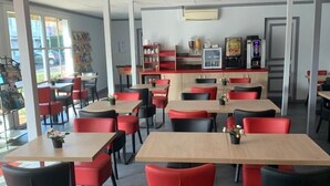 Interior moderno de restaurante com cadeiras vermelhas e pretas, mesas de madeira e um balcão com máquina de café.