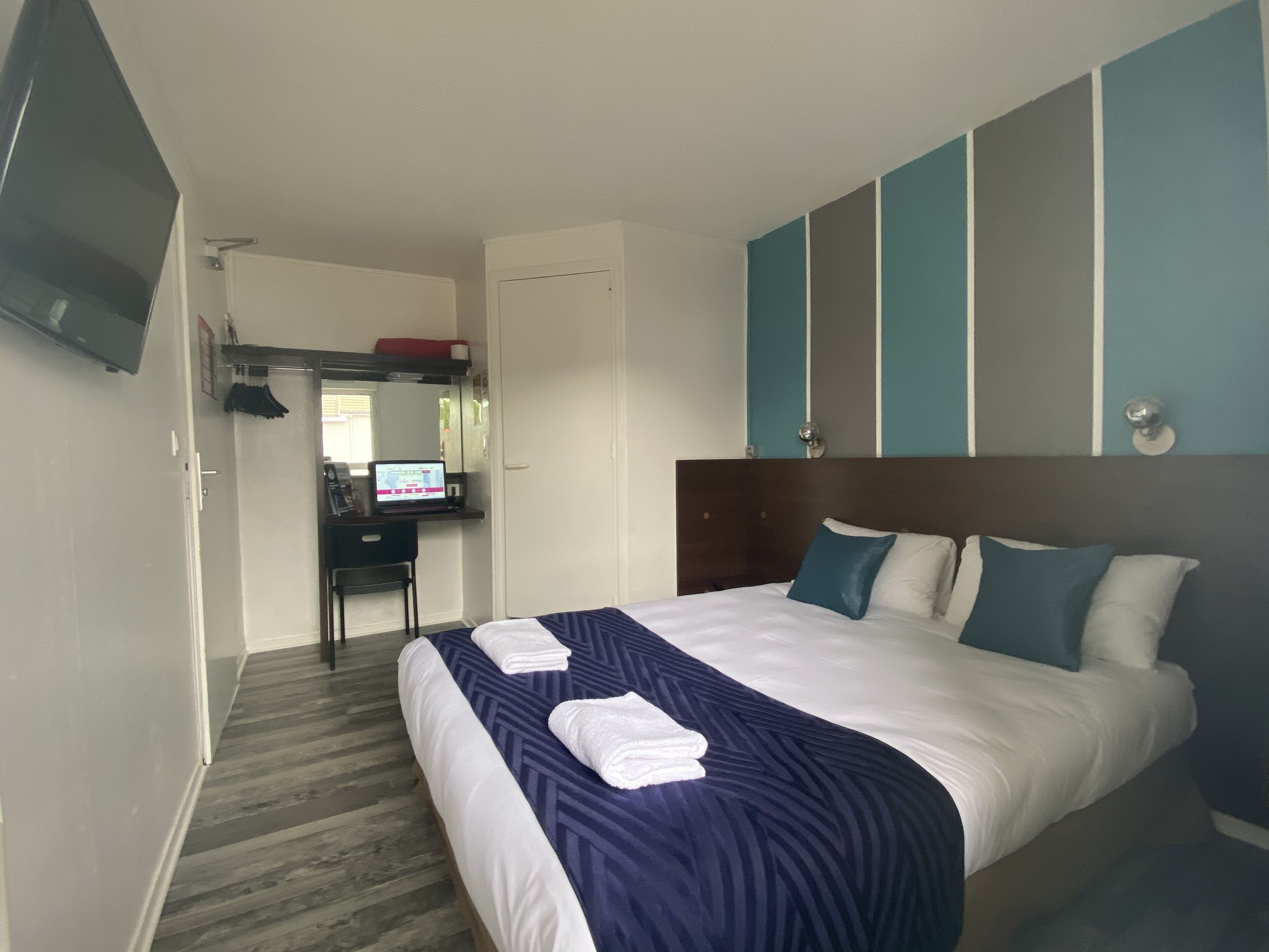Une chambre d’hôtel avec un lit, un bureau avec un ordinateur, une télévision et un miroir.