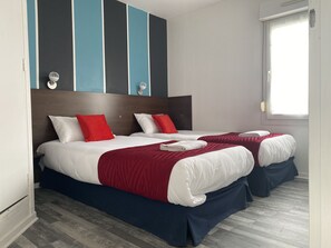 Una habitació d'hotel amb dos llits, cadascun amb roba de llit blanca i vermella, un panell de capçallet fosc i un disseny de paret amb ratlles.