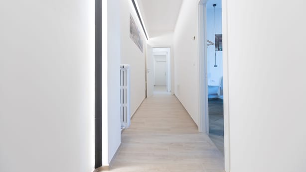 Un pasillo estrecho y bien iluminado con piso de tonos claros, que conduce a una puerta al final.