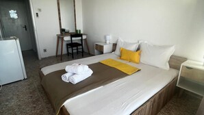 Habitación de hotel con una cama grande, un escritorio con silla, una mesita de noche con lámpara y un equipo de aire acondicionado en la pared.