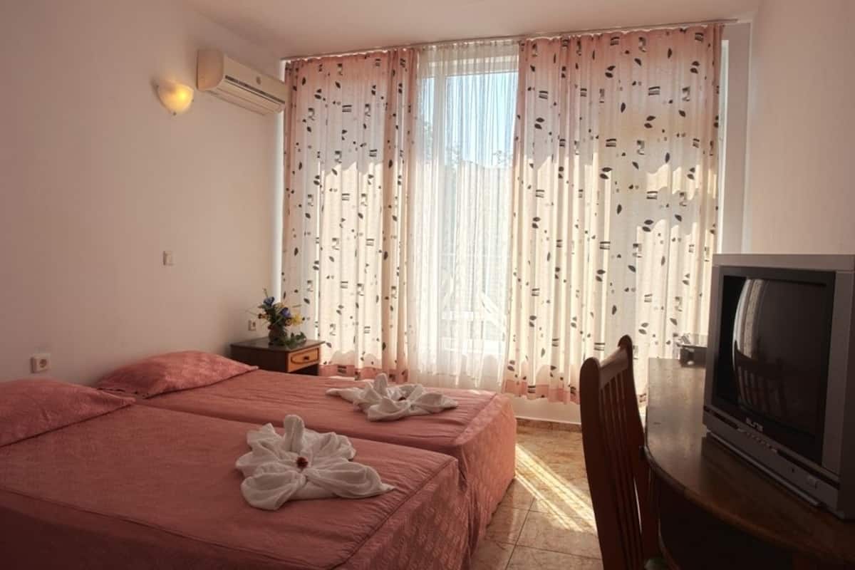 A hotel room with two beds, a TV, and a window with patterned curtains.