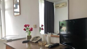 A hotel room with a wooden desk, a flat-screen TV, a telephone, a vase with flowers, and a window with curtains. - Sunny Varshava Hotel (Golden Sands)