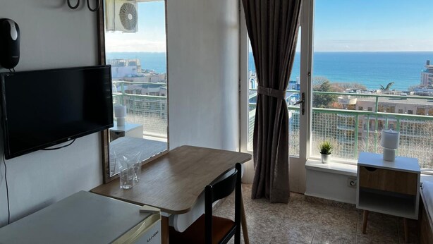 Habitación de hotel con un ventanal grande, un televisor de pantalla plana, una mesa de madera y un pequeño escritorio con lámpara.