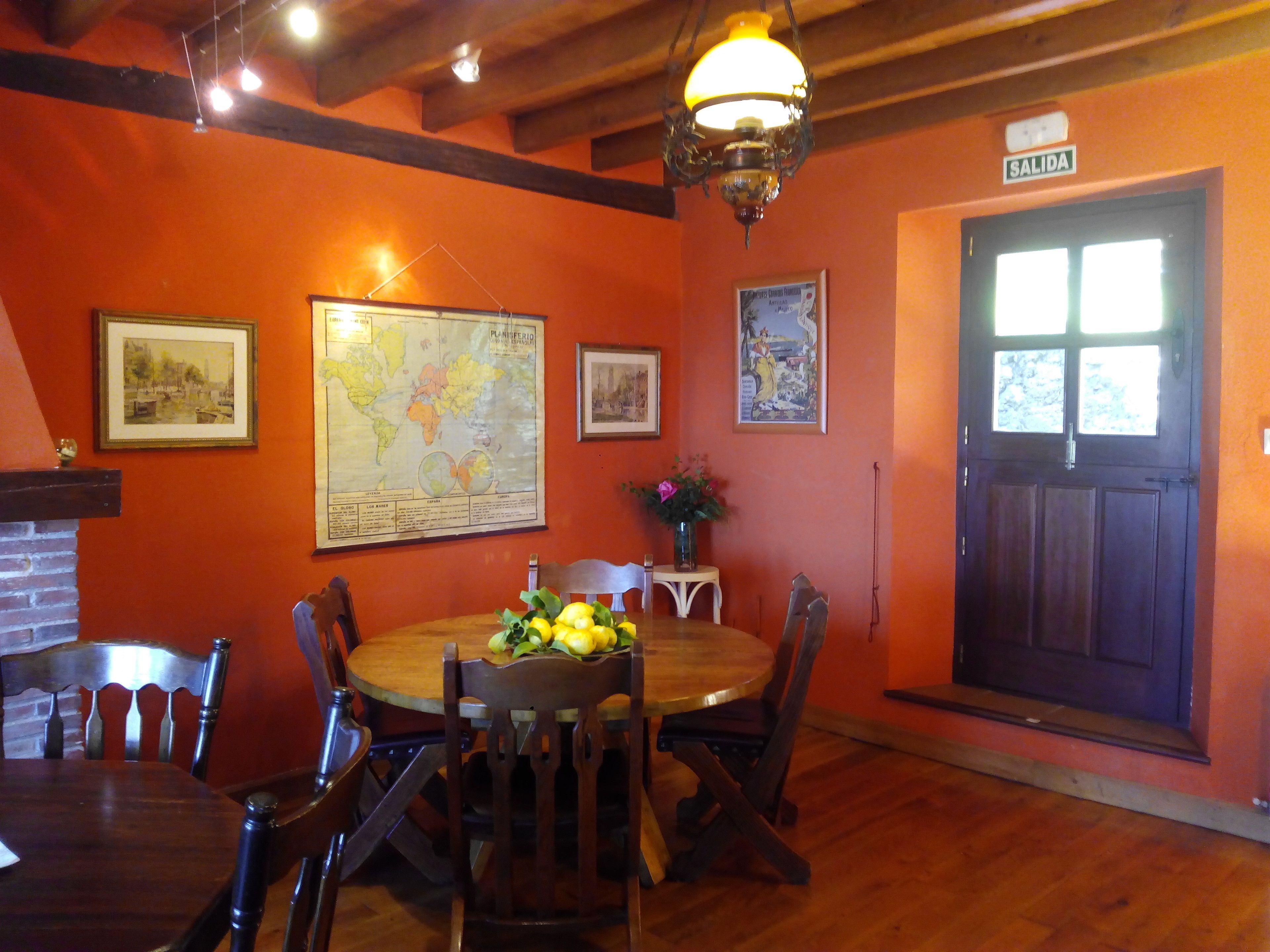 A dining area with a wooden table, chairs, a globe map, and a 'SALIDA' sign.