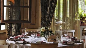 Une table à manger dressée pour un repas, avec des verres à vin, des assiettes et un centre de table composé de fleurs.