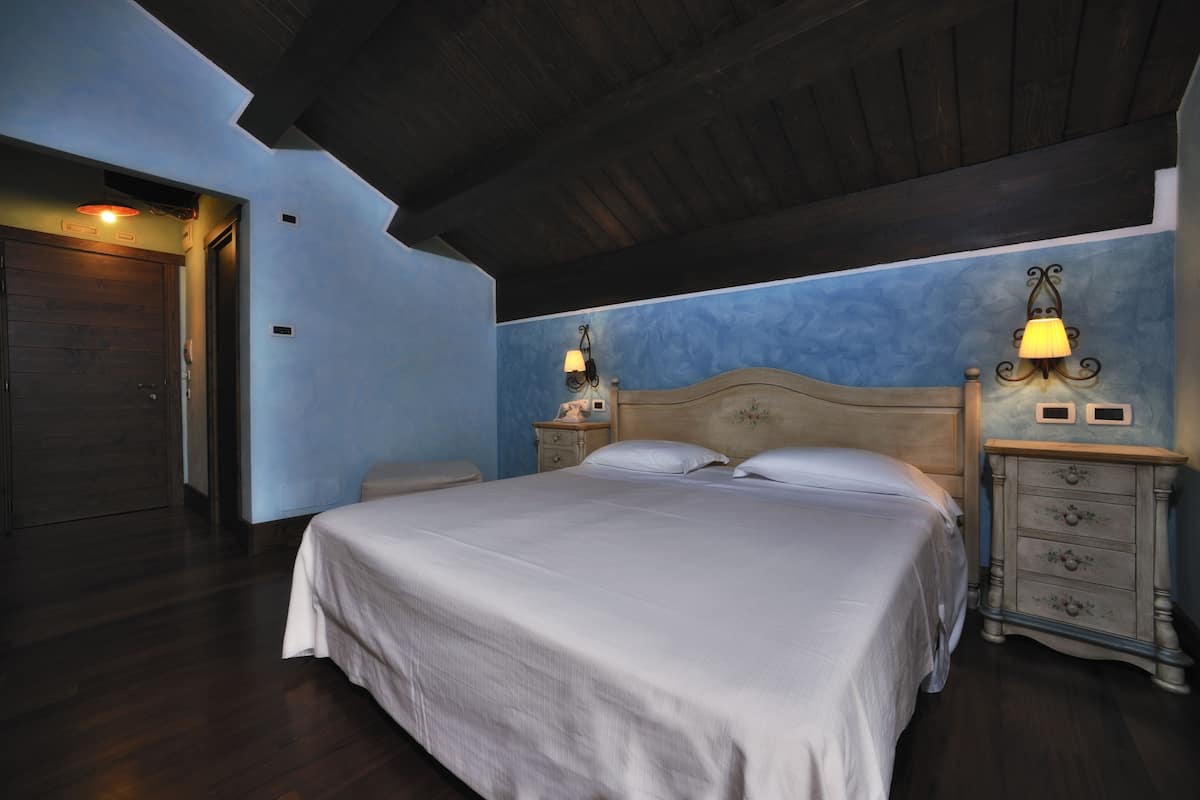 A bedroom with a large bed, wooden headboard, two bedside tables with lamps, a nightstand, and a wardrobe.