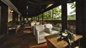 An indoor seating area with wooden tables and chairs, a view of trees through large windows, and a tiled floor. - Hotel Villa Danilo (Gamberale)