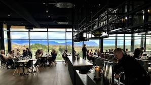 Un restaurante con amplios ventanales que ofrece vistas a montañas y un lago.