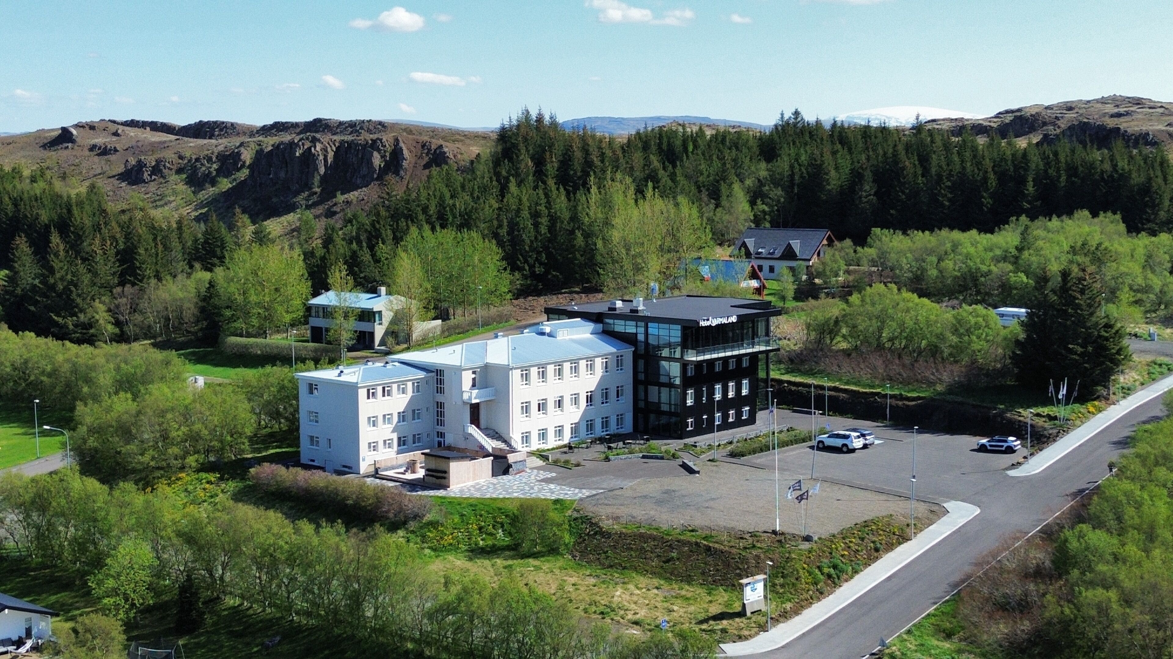 A modern hotel with a flat roof, surrounded by lush greenery and a mountainous backdrop.