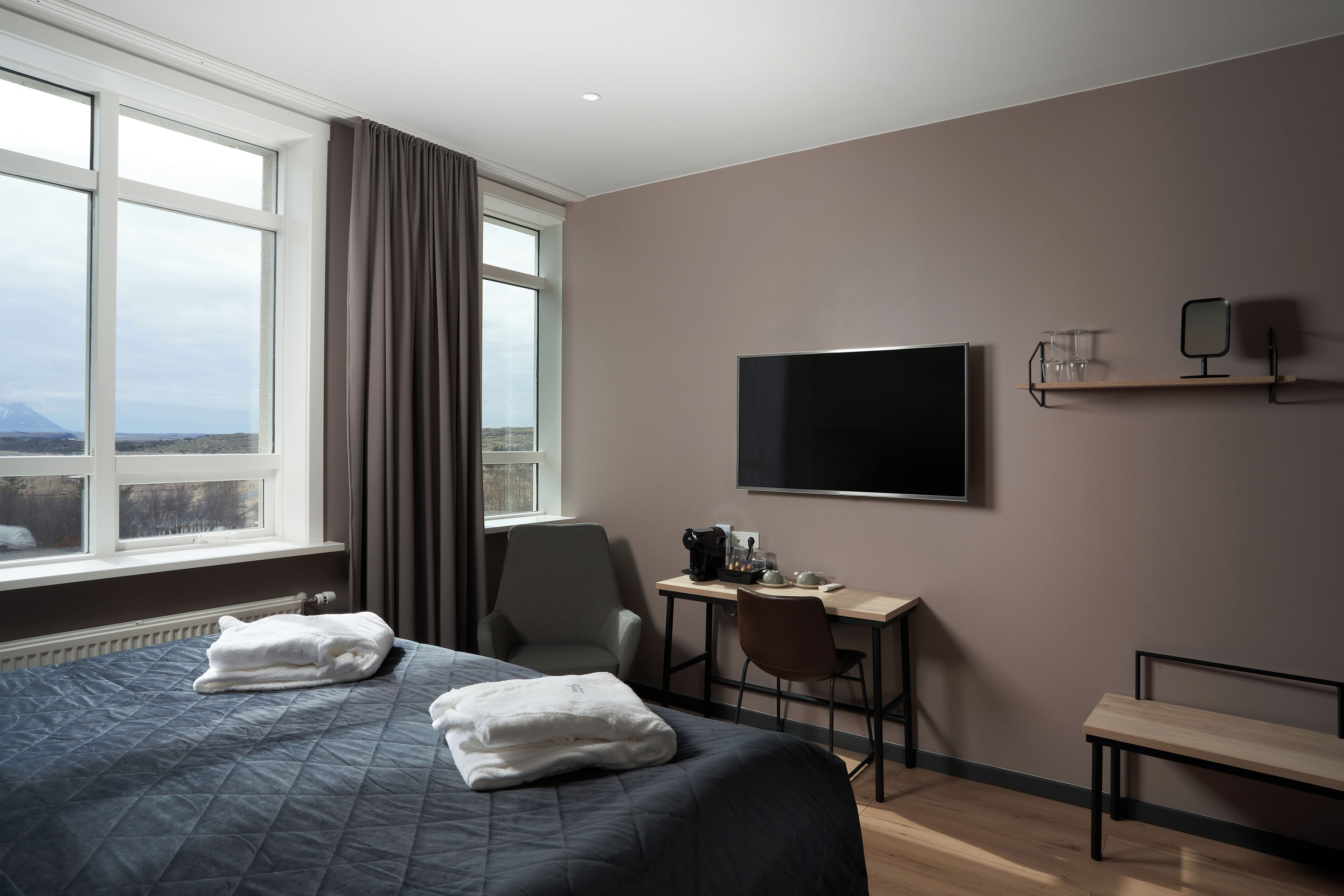 A hotel room with a large bed, a desk with a chair, a television, and a window with curtains.