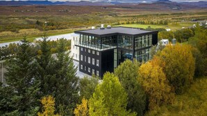 Un edificio moderno con fachada de vidrio, rodeado de follaje otoñal y un paisaje montañoso.