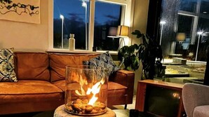 Una sala de estar con chimenea de vidrio, un sofá de cuero marrón, una mesa de centro redonda y un televisor.