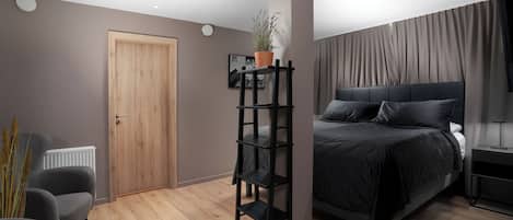 Un dormitorio moderno con una puerta de madera, un estante negro, una cama con ropa de cama oscura y un radiador.