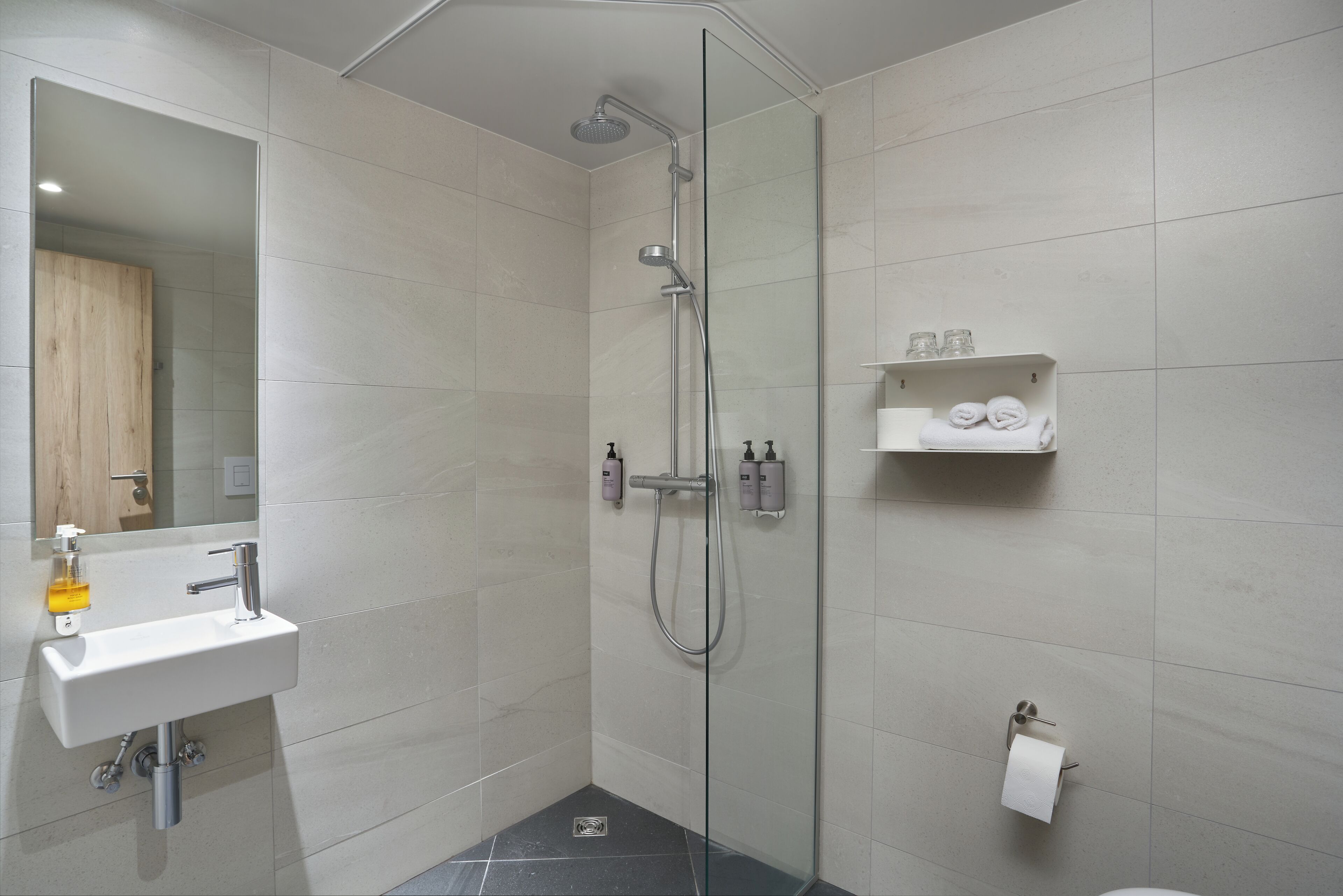 Une salle de bain moderne avec une douche à parois de verre, un lavabo blanc et une étagère contenant des articles de toilette.